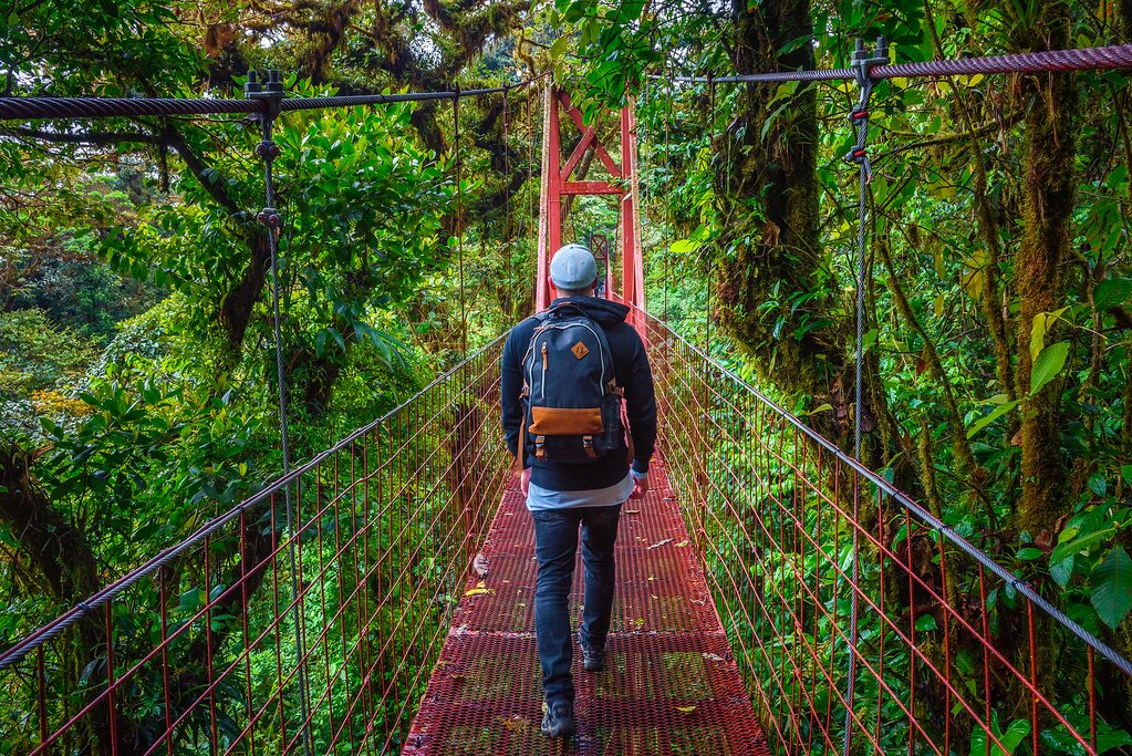 "Man with a backpack walking across a hanging bridge on a 7 days hiking itinerary in Costa Rica"
